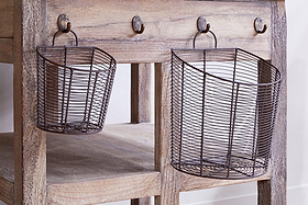 Two oval Inkollu Wall Hung Baskets (set of 2) by nkuku, in aged brass, are hung from hooks on a rustic wooden table with a naturally weathered finish and a lower shelf.
