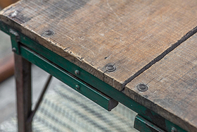 Close-up of the Ishan Reclaimed Folding Dining & Coffee Table by nkuku, showcasing its rustic wood grain, worn edges, and green metal frame. Grey and white patterned flooring is visible beneath the table.