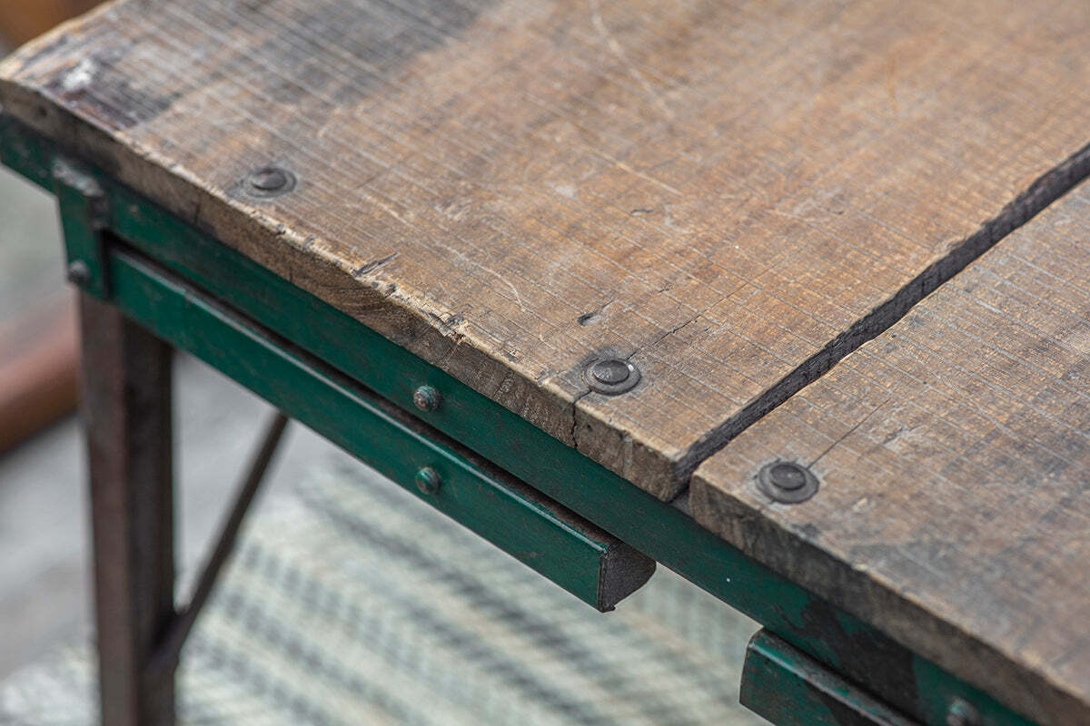Close-up of the Ishan Reclaimed Folding Dining & Coffee Table by nkuku, showcasing its rustic wood grain, worn edges, and green metal frame. Grey and white patterned flooring is visible beneath the table.