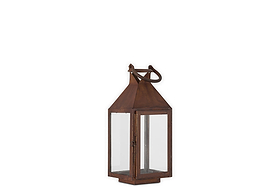 The Isko Lantern - Rust by nkuku features a vintage-style rectangular frame with clear glass panels, a rust finish, pointed top, metal loop handle, and flat base—ideal for pillar candles or adding rustic charm to your garden seating.
