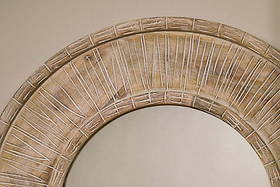 Close-up of the Itwa Mango Wood Carved Mirror by nkuku. The top section highlights a wide, textured frame of hand-carved mango wood with linear radial grooves, set against a neutral beige wall for a rustic, artisanal touch.