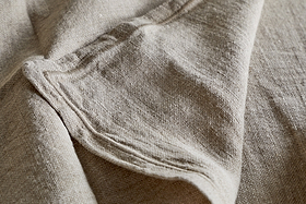 Close-up of the nkuku Junto Linen Napkin - Natural (Set of 4): beige, textured linen with visible folds and seams, highlighting its natural weave—perfect for a neutral table setting.