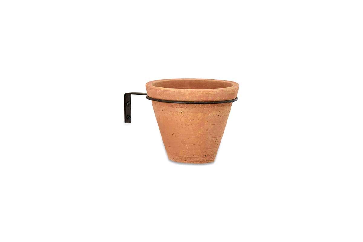 The nkuku Jara Single Wall Hung Planter features a classic, unglazed terracotta pot with a tapered shape, held by a black metal bracket for a sleek look against a plain white background.