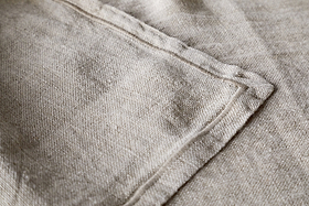 A close-up of the Junto Linen Runner - Natural (Large) by nkuku highlights its beige linen fabric, visible stitching, and neatly sewn seam for a refined, neutral table runner.