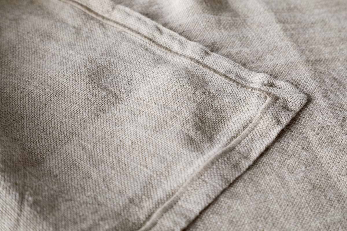 A close-up of the Junto Linen Runner - Natural (Large) by nkuku highlights its beige linen fabric, visible stitching, and neatly sewn seam for a refined, neutral table runner.