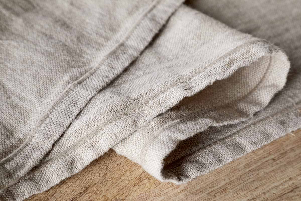 Close-up of the nkuku Junto Linen Runner in Natural (Large), showing its durable texture and visible seams, neatly folded on wood—a versatile neutral table runner for any decor.