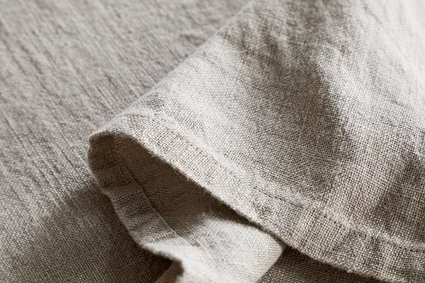 Close-up of the nkuku Junto Linen Tablecloth in Natural (Large), showcasing its beige, textured linen and natural weave—durable and elegant with a neatly folded section for refined table settings.