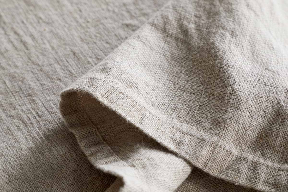 Close-up of the nkuku Junto Linen Tablecloth in Natural (Large), showcasing its beige, textured linen and natural weave—durable and elegant with a neatly folded section for refined table settings.