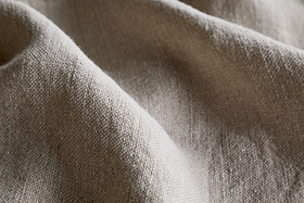 Close-up of the Junto Linen Tablecloth in Natural by nkuku, featuring a beige, textured weave with soft folds and gentle shadows—a versatile, neutral large tablecloth perfect for any setting.