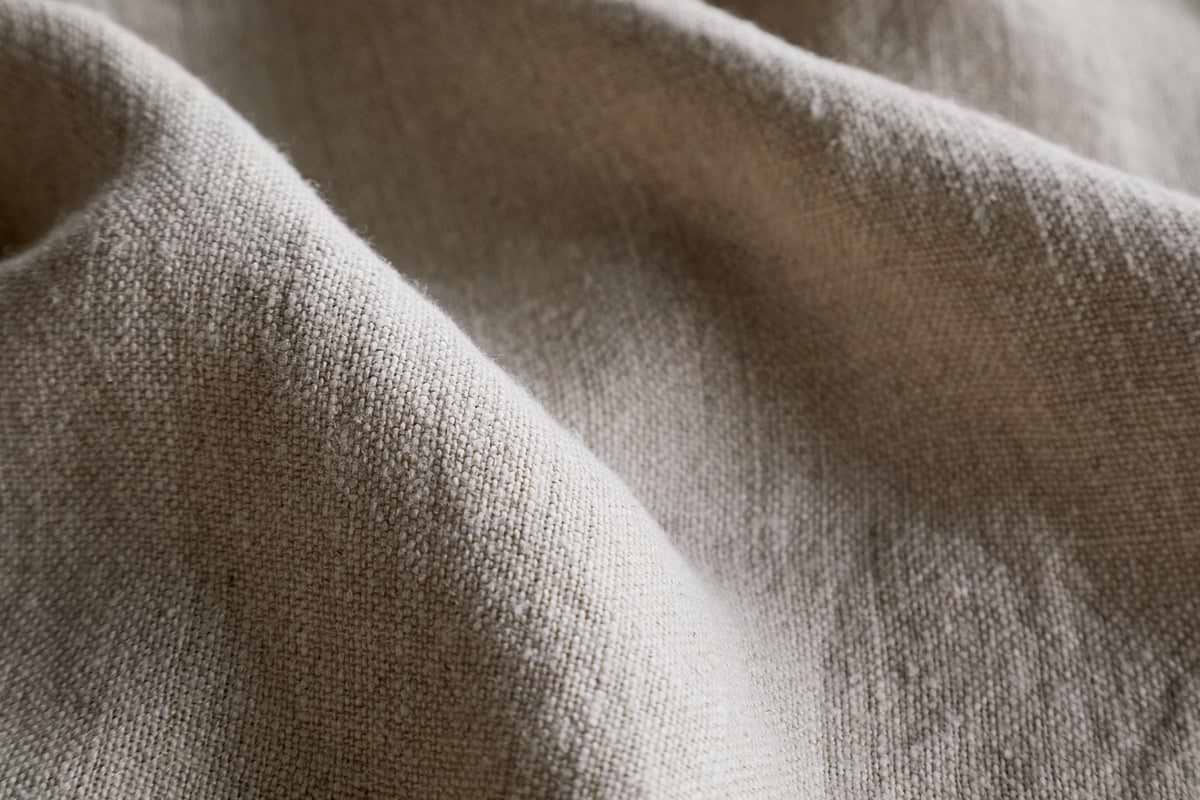 Close-up of the Junto Linen Tablecloth in Natural by nkuku, featuring a beige, textured weave with soft folds and gentle shadows—a versatile, neutral large tablecloth perfect for any setting.