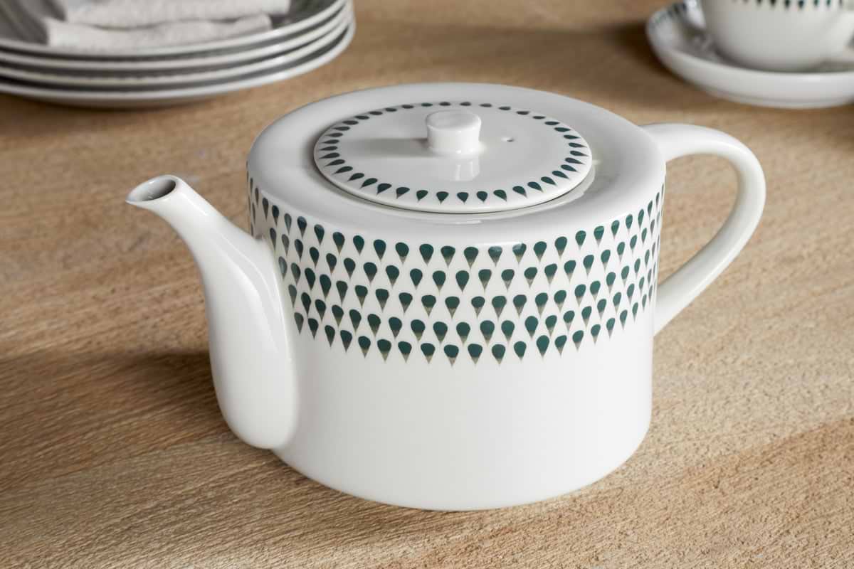 The nkuku Juniper Drop 4 Person Teapot in Cream & Juniper, featuring green teardrop patterns, sits on a wooden table with matching plates and cup—the ideal gift for tea lovers.