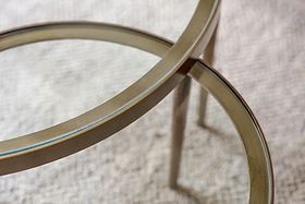 Close-up of two nkuku Jiya Iron & Glass Nested Coffee Tables - Brass, featuring round glass tops and slim brass rims, elegantly overlapping on a light textured carpet to showcase their refined edges and legs.