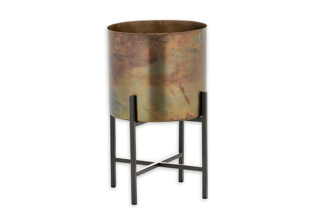 The Juoni Iron Planter by nkuku features a cylindrical iron pot in a mottled brass holder, elevated on a tall black metal stand with four legs and crossbars—ideal for showcasing house plants in modern, industrial style.