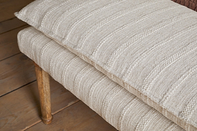 The Kiana Cotton Upholstered Bench by nkuku features a beige, textured cushion with subtle stripes and wooden legs, creating a stylish accent piece for any wooden floor.