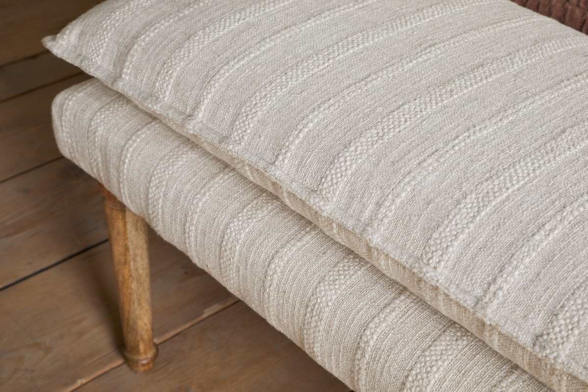 The Kiana Cotton Upholstered Bench by nkuku features a beige, textured cushion with subtle stripes and wooden legs, creating a stylish accent piece for any wooden floor.