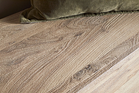 Close-up of the Karadi Reclaimed Wood Storage Bench - Natural by nkuku, featuring visible grain patterns beside a green velvet cushion. The mix of textured wood and soft pillow brings a warm, cozy feel to the space.