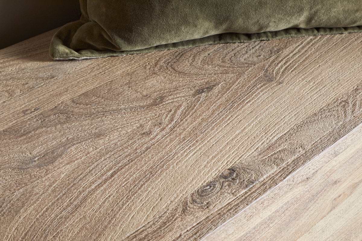 Close-up of the Karadi Reclaimed Wood Storage Bench - Natural by nkuku, featuring visible grain patterns beside a green velvet cushion. The mix of textured wood and soft pillow brings a warm, cozy feel to the space.