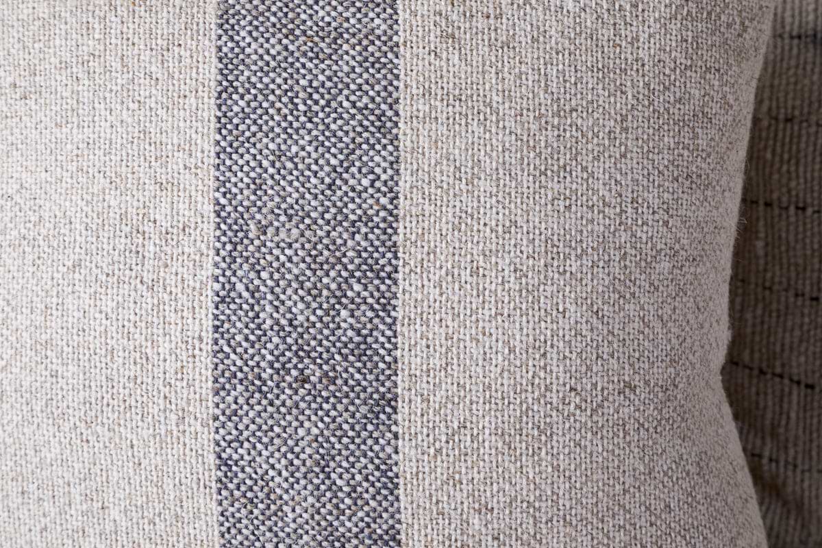 A close-up of the nkuku Kallu Wool & Cotton Cushion Cover - Natural, featuring a visible coarse weave and a vertical dark gray stripe running down the center.
