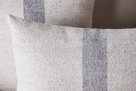 Two nkuku Kallu Wool & Cotton Cushion Covers in natural are shown overlapping, featuring a vertical blue-grey stripe pattern that highlights their woven texture and minimalist design.