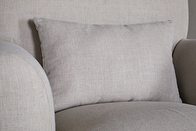 A close-up of the nkuku Kashi Linen Armchair in natural features textured light gray linen fabric and a matching rectangular cushion against the backrest.