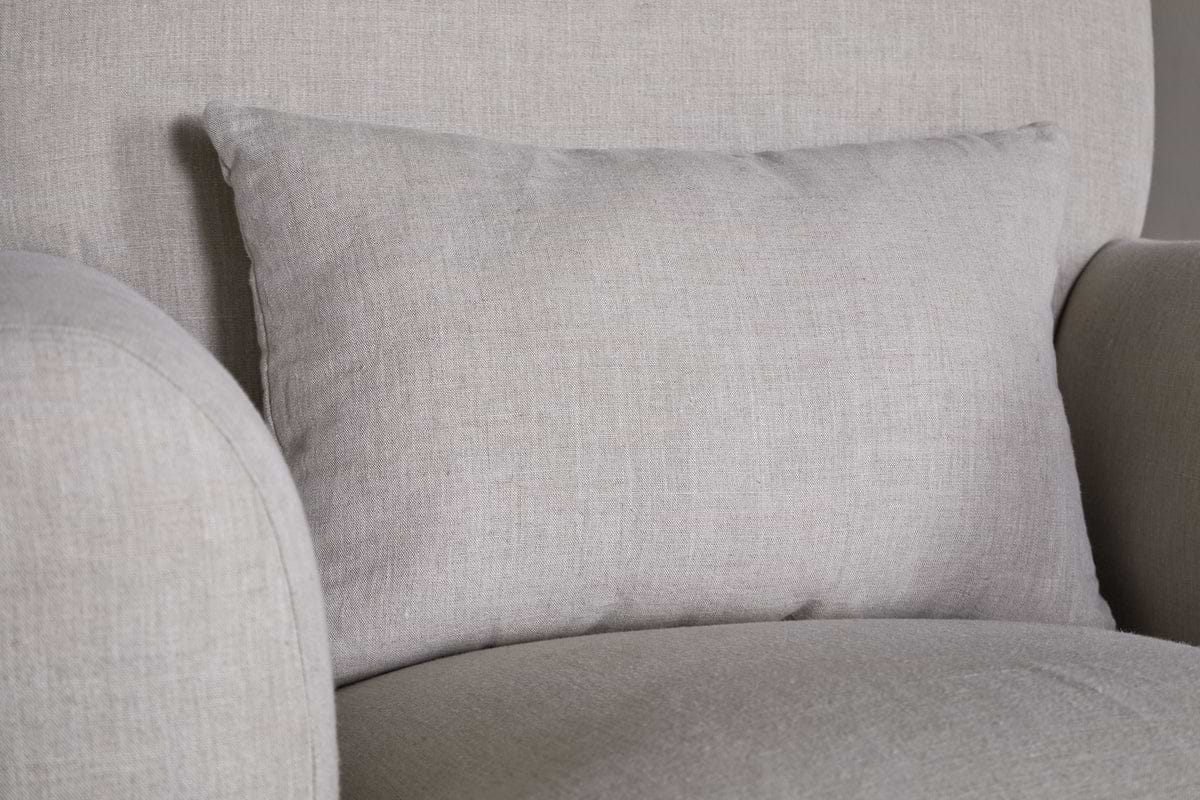 A close-up of the nkuku Kashi Linen Armchair in natural features textured light gray linen fabric and a matching rectangular cushion against the backrest.