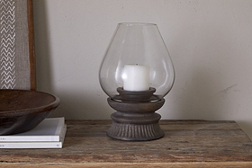 A white rustic pillar candle is placed inside the nkuku Kawani Mango Wood Lantern - Dark Ash on a wooden table, accompanied by stacked books and a wooden bowl.