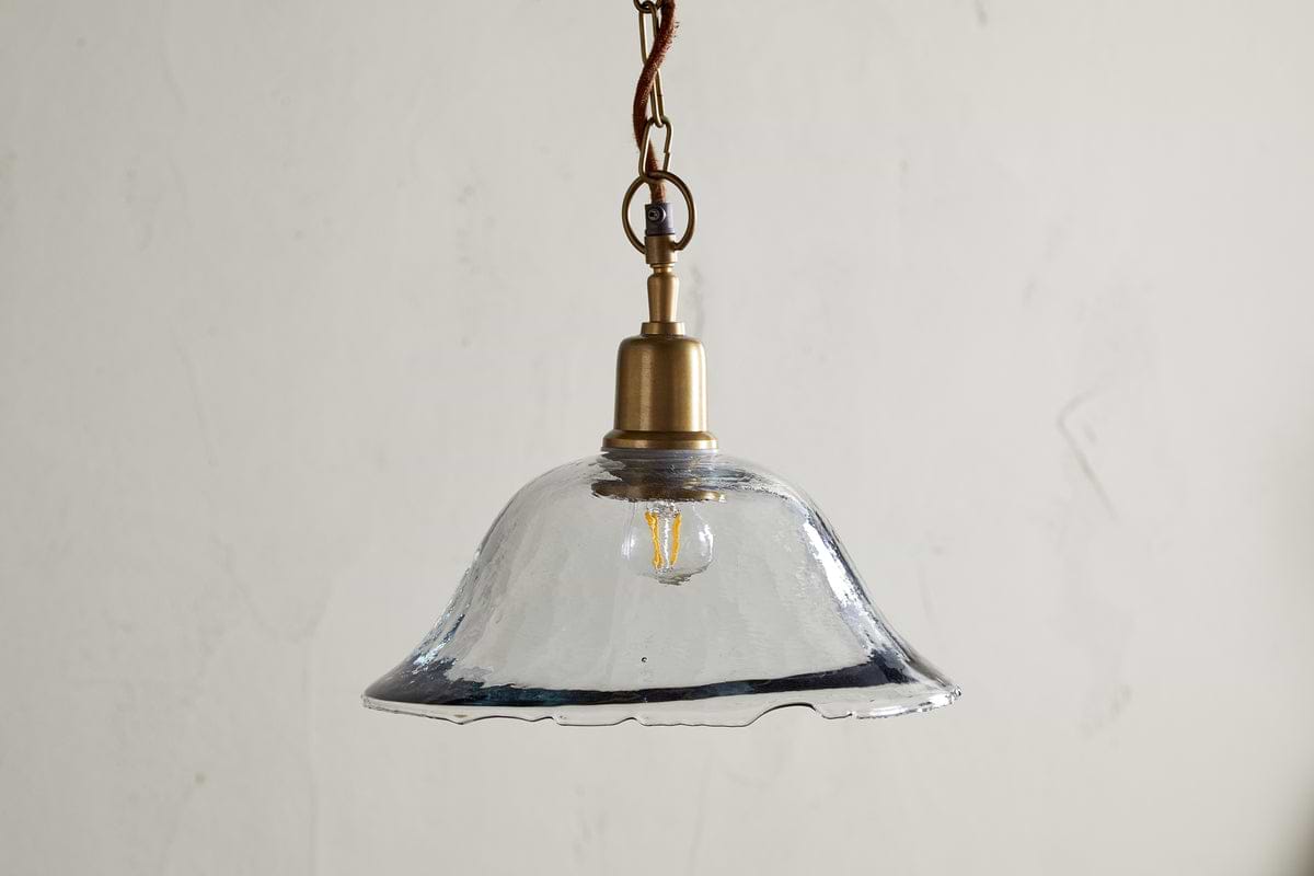 The Keju Organic Shape Recycled Glass Pendant in clear by nkuku features a stylish glass shade suspended from a chain, bringing elegant flair to any room.