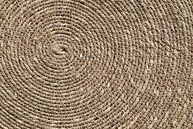Close-up of the nkuku Keso Woven Placemats - Brown (Set of 4) reveals detailed circular and spiral patterns in natural fibers—perfect as a textured, handcrafted backdrop for minimalist tableware or handwoven coasters.