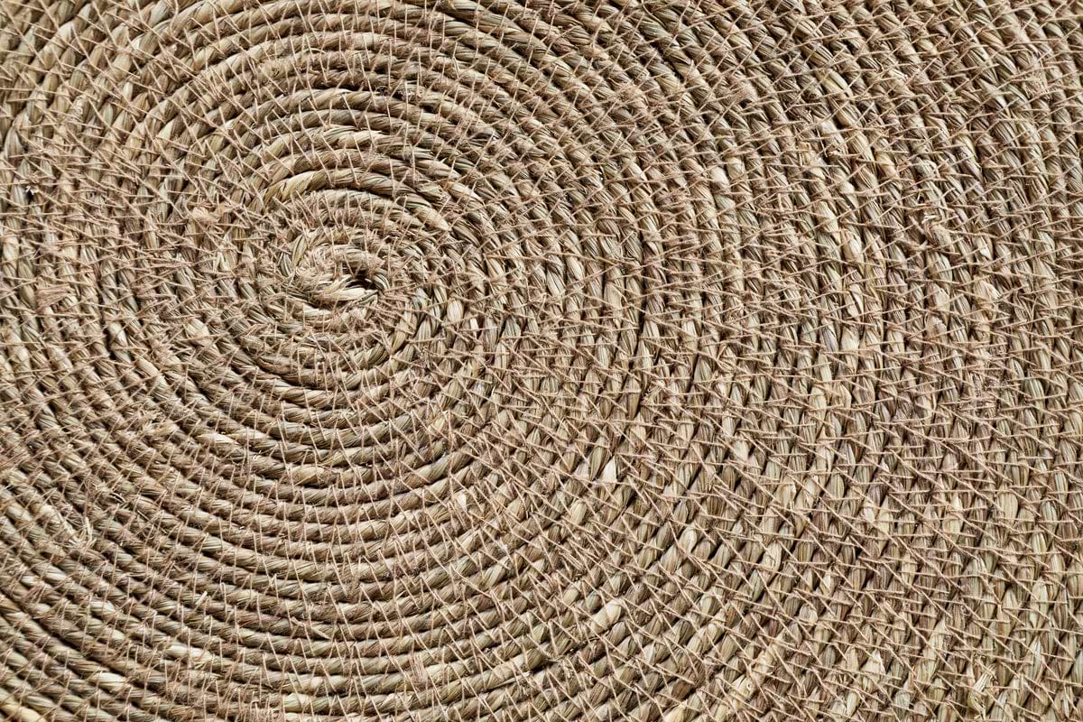 Close-up of the nkuku Keso Woven Placemats - Brown (Set of 4) reveals detailed circular and spiral patterns in natural fibers—perfect as a textured, handcrafted backdrop for minimalist tableware or handwoven coasters.