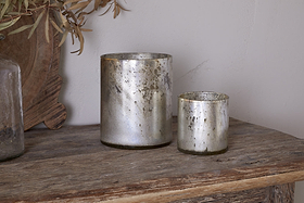 Two metallic Kunjari Tealight Holders - Rustic Gold by nkuku in different sizes are displayed on a rustic wooden surface with olive branches—ideal for showcasing recycled glass tealights against a light wall.