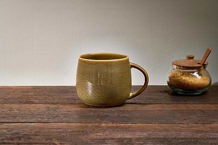 An extra large, green Kalini Mug by nkuku sits on a wooden table beside a glass jar of brown sugar and a wooden spoon.