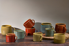 A set of two large, handmade Kalini Mugs in green by nkuku, styled on a rustic wooden surface with a neutral wall background.