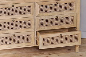 The Kanz Mango Wood Chest Of Drawers by nkuku features cane-paneled drawers with small round brass knobs, crafted from light mango wood—perfect bedroom storage. One drawer is shown partially open to reveal its spacious interior.