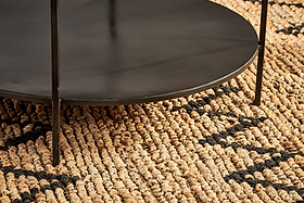 Close-up of the Karoko Marble Coffee Table by nkuku, featuring thin legs, set on a woven jute rug. The thick natural fibers and black geometric pattern of the rug contrast with the table's smooth, contemporary marble top.