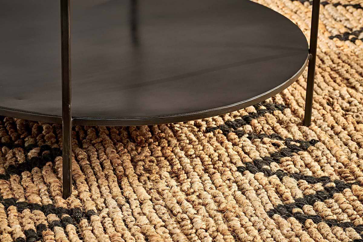 Close-up of the Karoko Marble Coffee Table by nkuku, featuring thin legs, set on a woven jute rug. The thick natural fibers and black geometric pattern of the rug contrast with the table's smooth, contemporary marble top.
