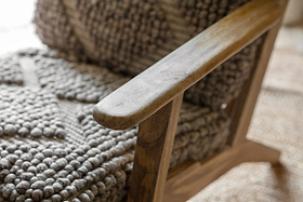 Close-up of the Keya Chunky Weave & Mango Wood Chair - Natural by nkuku, showing its rustic mango wood armrest and chunky-weave wool upholstery, which create a striking contrast of textures in this stylish occasional chair.