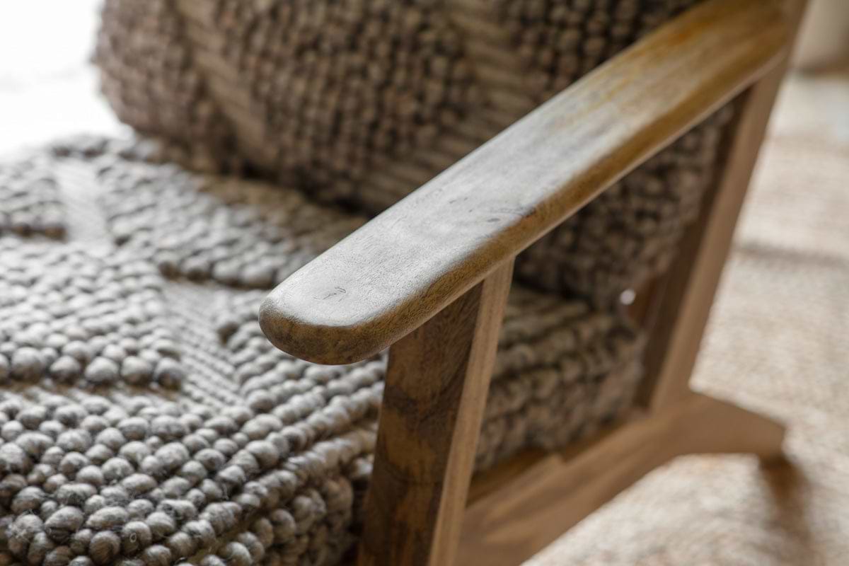 Close-up of the Keya Chunky Weave & Mango Wood Chair - Natural by nkuku, showing its rustic mango wood armrest and chunky-weave wool upholstery, which create a striking contrast of textures in this stylish occasional chair.