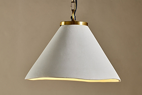 The Kiara Organic Shape Ceramic Pendant Light by nkuku features a wide, wavy-edged off-white shade and antique brass chain, creating a handcrafted modern look against a taupe backdrop.