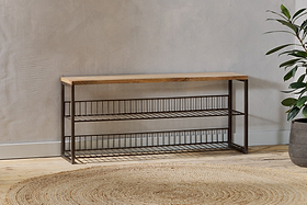 The Kiyoma Iron & Wood Low Standing Shelves – Natural by nkuku features a mango wood top and three wire shelves, adding industrial style to your space when placed against a textured gray wall.