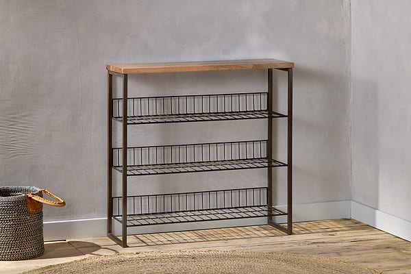 The nkuku Kiyoma Iron & Wood Tall Standing Shelves - Natural stand against a light gray wall on a wooden floor, combining minimalist and industrial style. A woven basket sits to the left, with a round woven rug partially in front.
