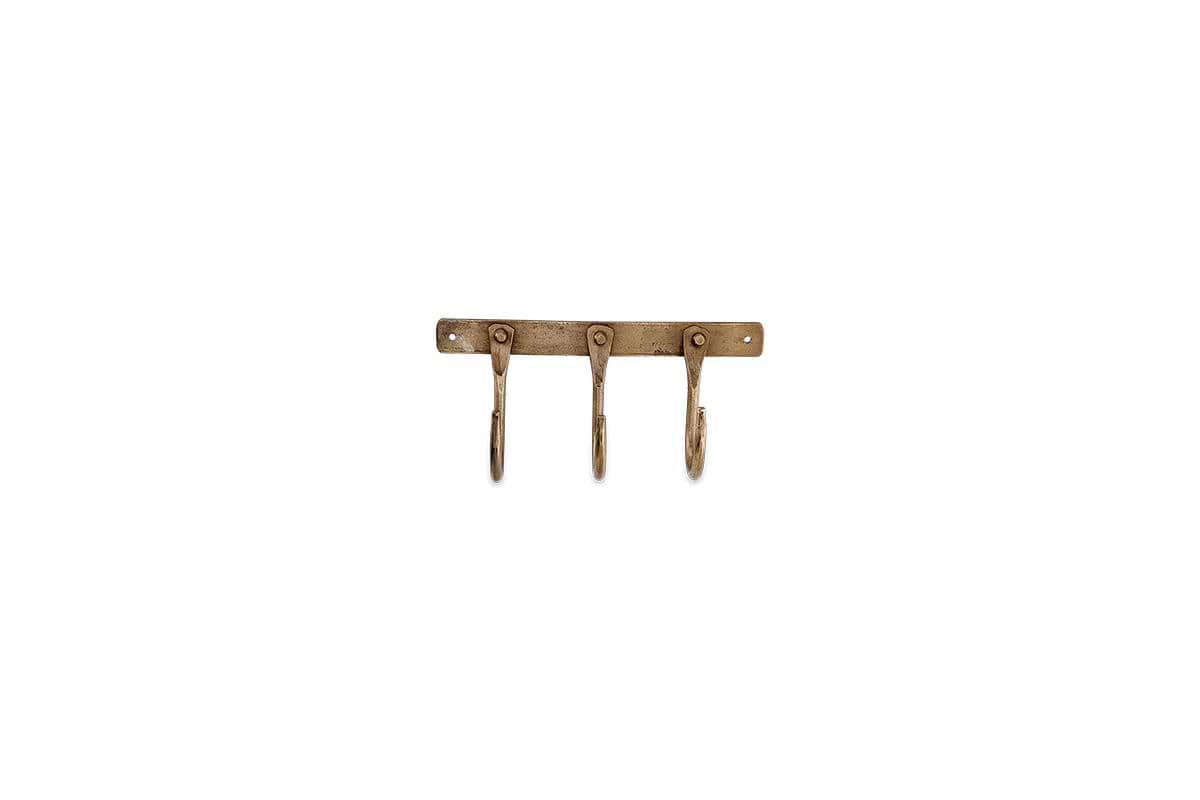 The nkuku Kuna Iron Hooks - Antique Brass features three vintage, curved iron hooks on a rectangular wall-mounted base with two visible screw holes, ideal for adding stylish, small storage to any space.