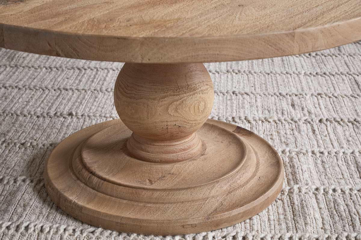 Close-up of the nkuku Laya Round Carved Coffee Table – Natural, showcasing its sculptural form, raw wood finish, and natural grain atop a textured beige striped rug.