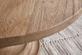 Close-up of the nkuku Laya Round Carved Coffee Table in a natural finish, highlighting its distinctive grain, placed atop a light woven rug with visible stitching.