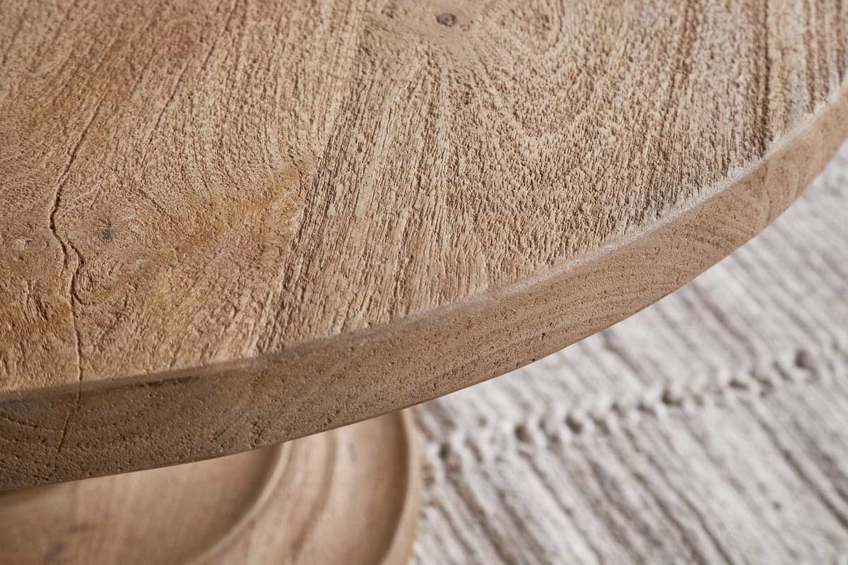 Close-up of the nkuku Laya Round Carved Coffee Table in a natural finish, highlighting its distinctive grain, placed atop a light woven rug with visible stitching.