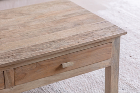 A close-up of the Laali Grooved Mango Wood Coffee Table by nkuku shows its hand-carved rectangular top, simple drawer with wooden handle, and slender legs. Made from sustainable mango wood, it stands over a light textured carpet in soft lighting.