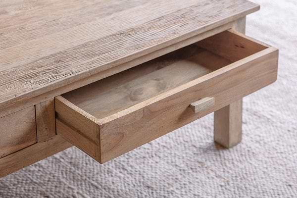 A close-up of the nkuku Laali Grooved Mango Wood Coffee Table - Natural shows its minimal, rustic design and hand-carved detail. An open drawer reveals the light mango wood grain against a textured beige carpet.