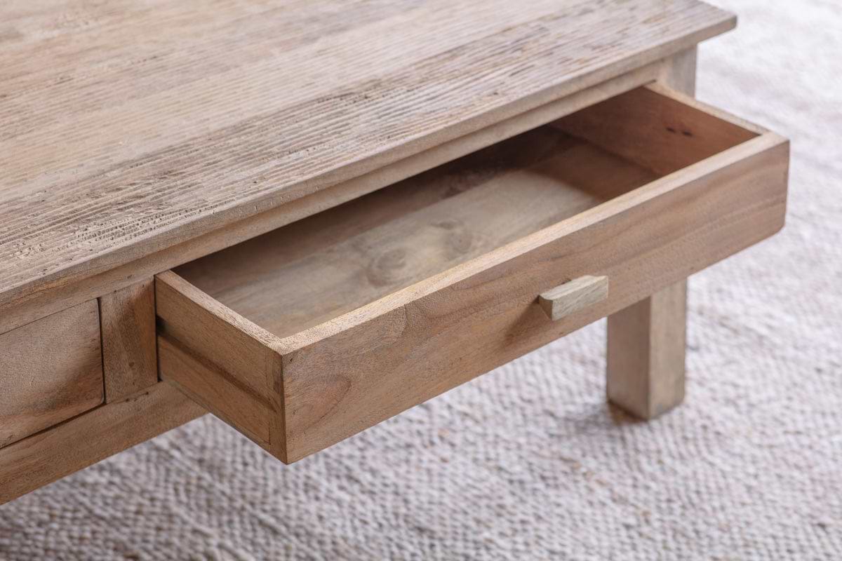 A close-up of the nkuku Laali Grooved Mango Wood Coffee Table - Natural shows its minimal, rustic design and hand-carved detail. An open drawer reveals the light mango wood grain against a textured beige carpet.