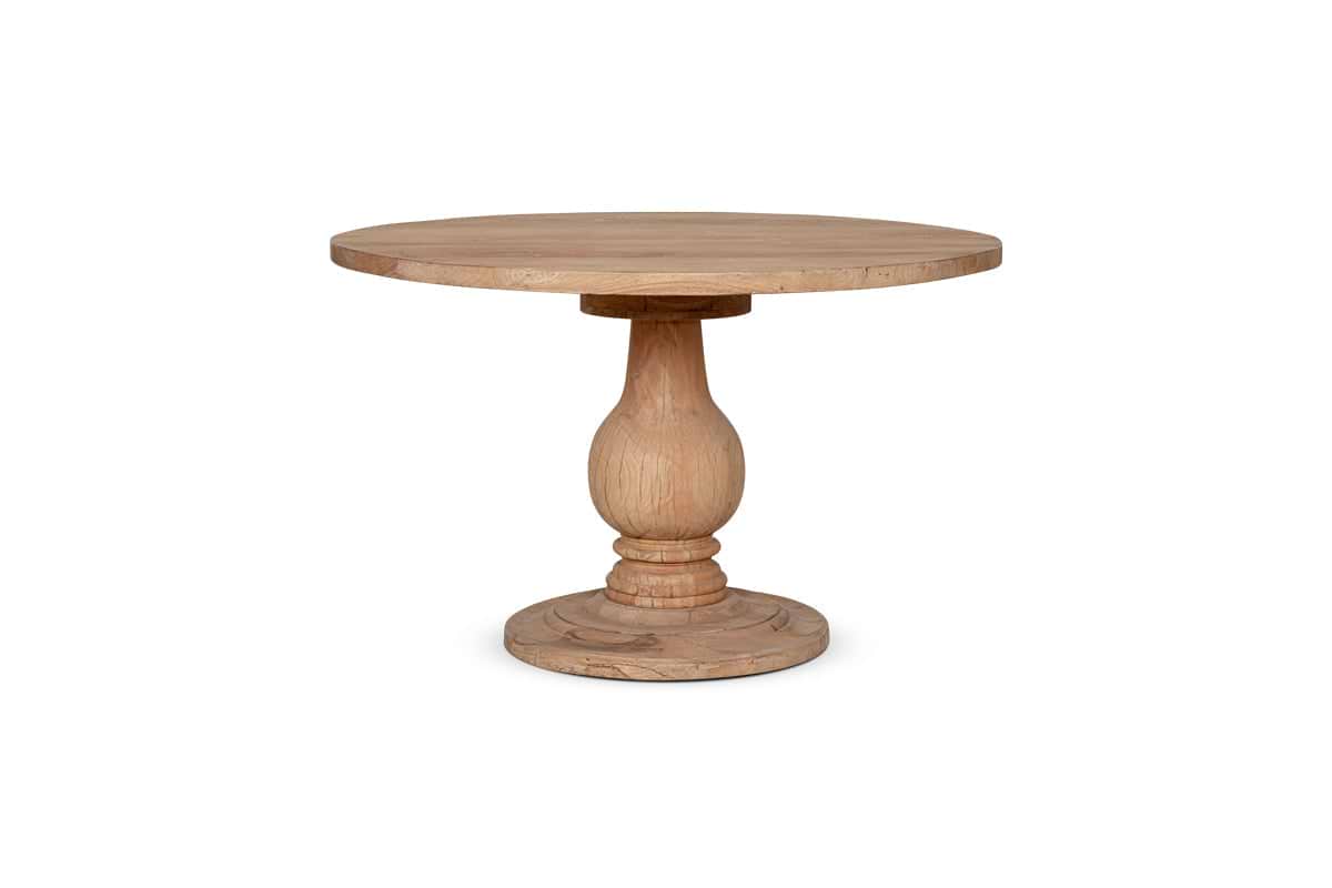 The nkuku Laya Round Carved Mango Wood Table - Small features a smooth, natural light-finished top and a single thick, hand-carved pedestal base, shown on a solid base against a white background.