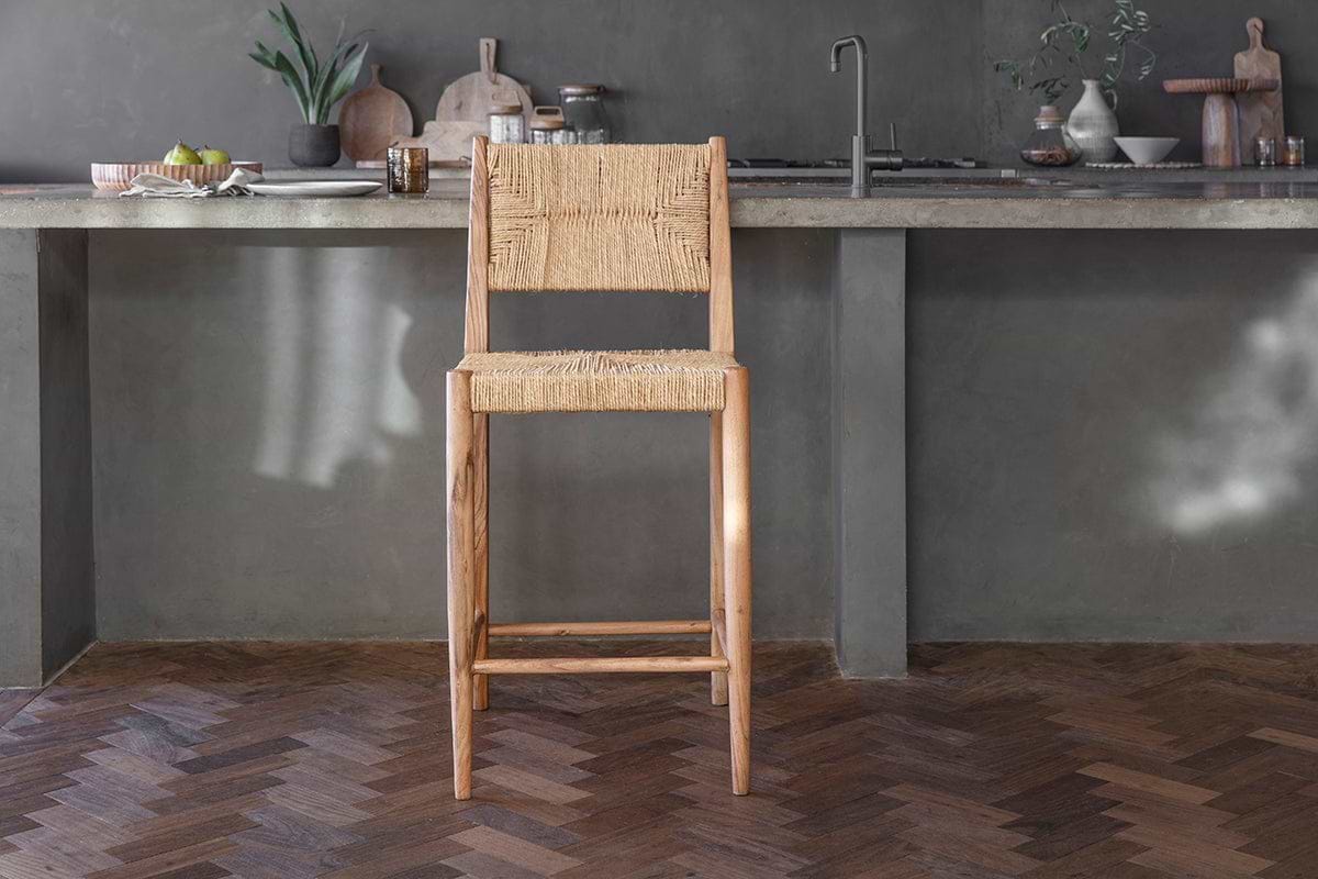 The Lohanda Acacia & Munja Grass Counter Chair by nkuku features a handcrafted light acacia wood frame with a square seat and back elegantly woven from natural munja grass, perfect for pairing with a concrete kitchen island.