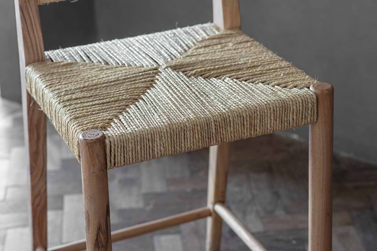 The nkuku Lohanda Acacia & Munja Grass Counter Chair features a handcrafted acacia frame and a seat intricately woven from natural beige munja grass, highlighting artisanal craftsmanship and elegant geometric patterns.